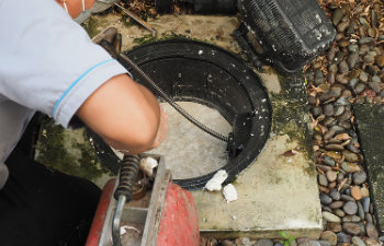Plumber repairing clogged grease trap with auger machine